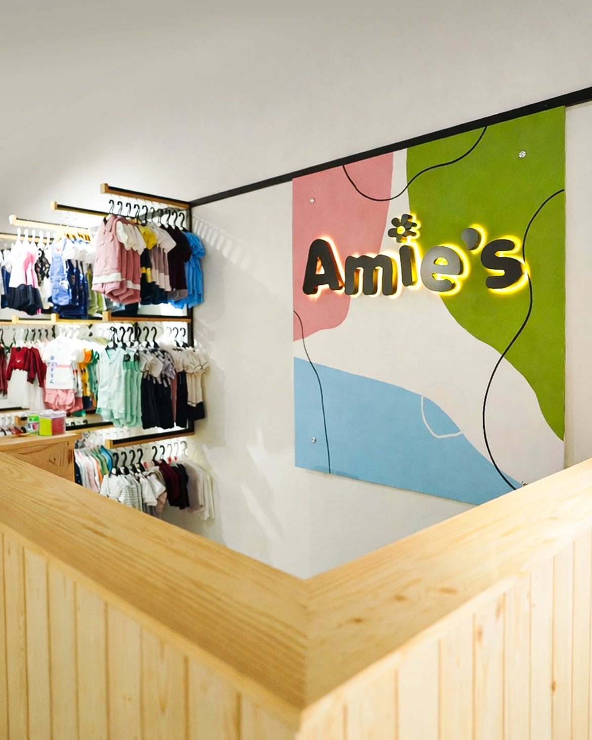 Color-blocked Amie's wall sign above a pale wood counter, with clothing racks beyond