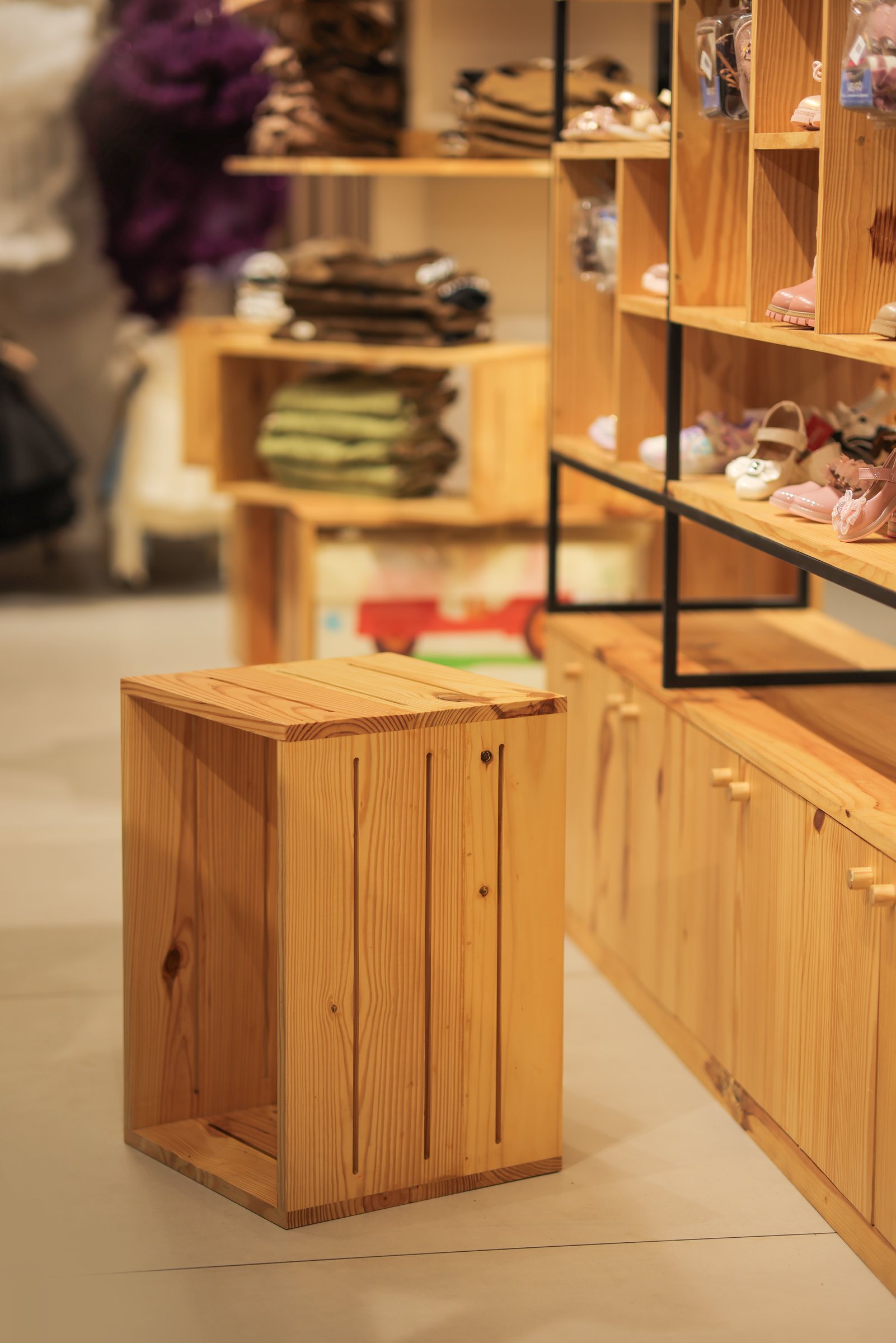 Slatted wood display cube beside illuminated shelves of folded clothes and shoes